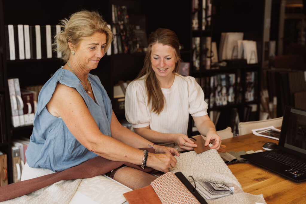 Twee vrouwen bekijken stofstalen aan een tafel in de showroom